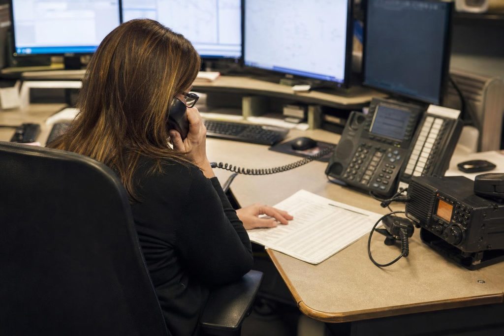 Communications coordinator checking incident notes while consulting someone by telephone in an operations room.