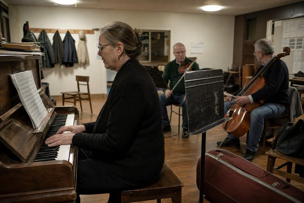 Adult musician practicing piano with a small ensemble in a rehearsal room.