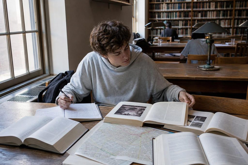 Student exploring books from several subjects at a university library table.